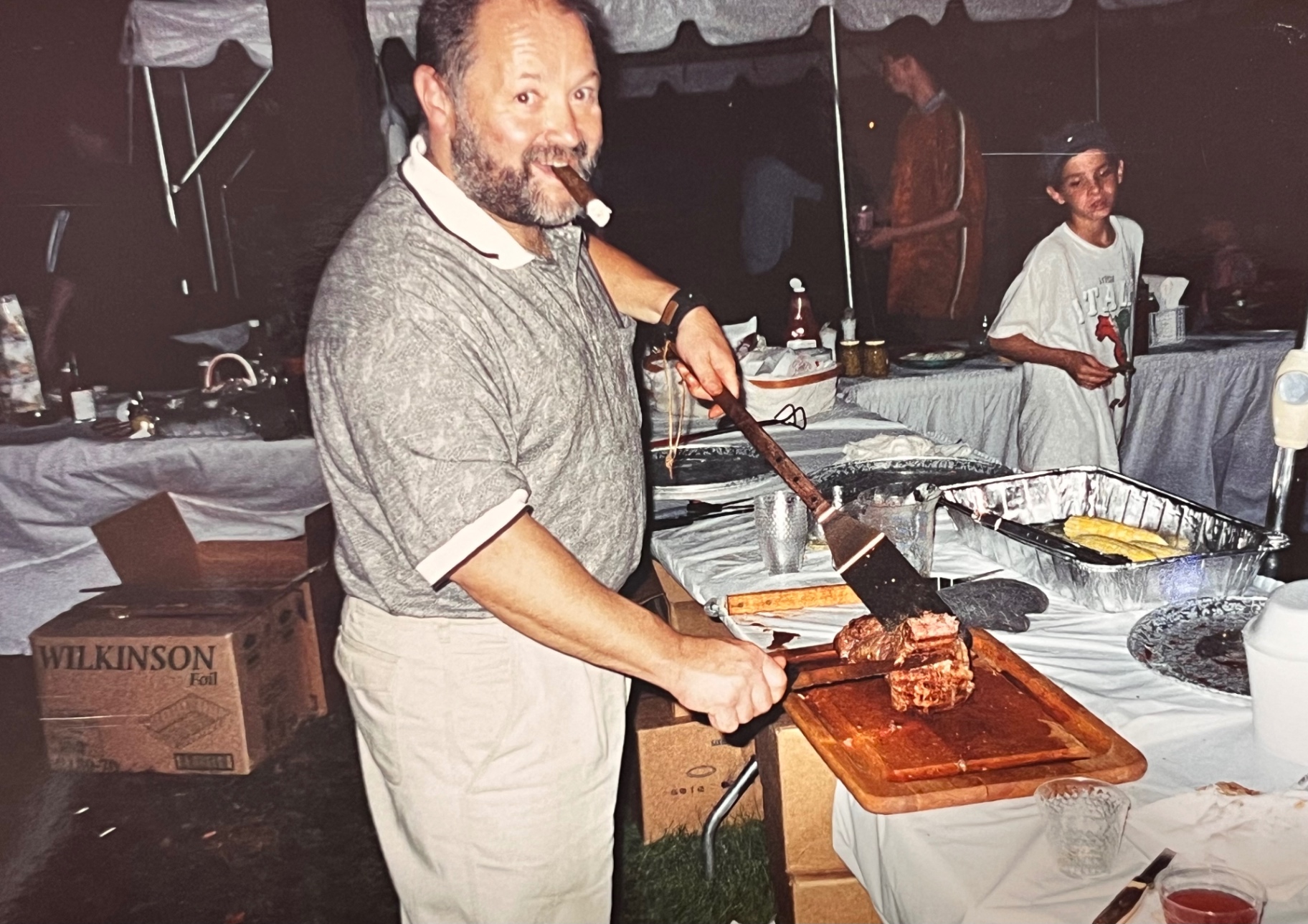 Carving the roast — cigar in hand, apron on, the pit master at work