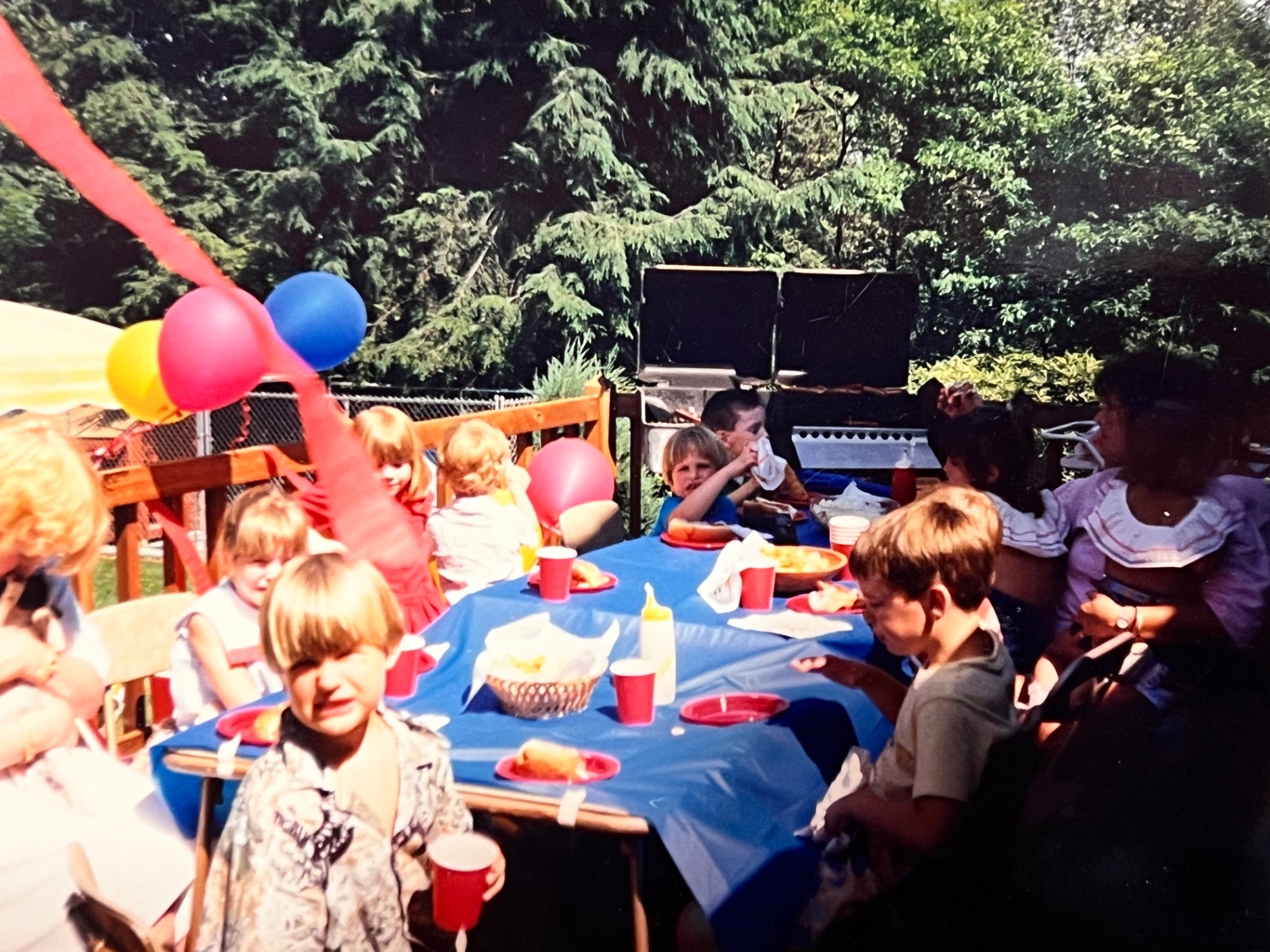 Backyard cookout birthday — balloons, blue tablecloth, the whole gang around the picnic table