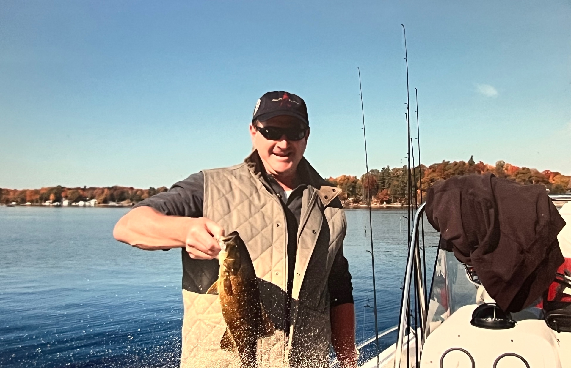 Richard in the quilted vest, holding a bronze-backed beauty — fall color blazing across the far shore