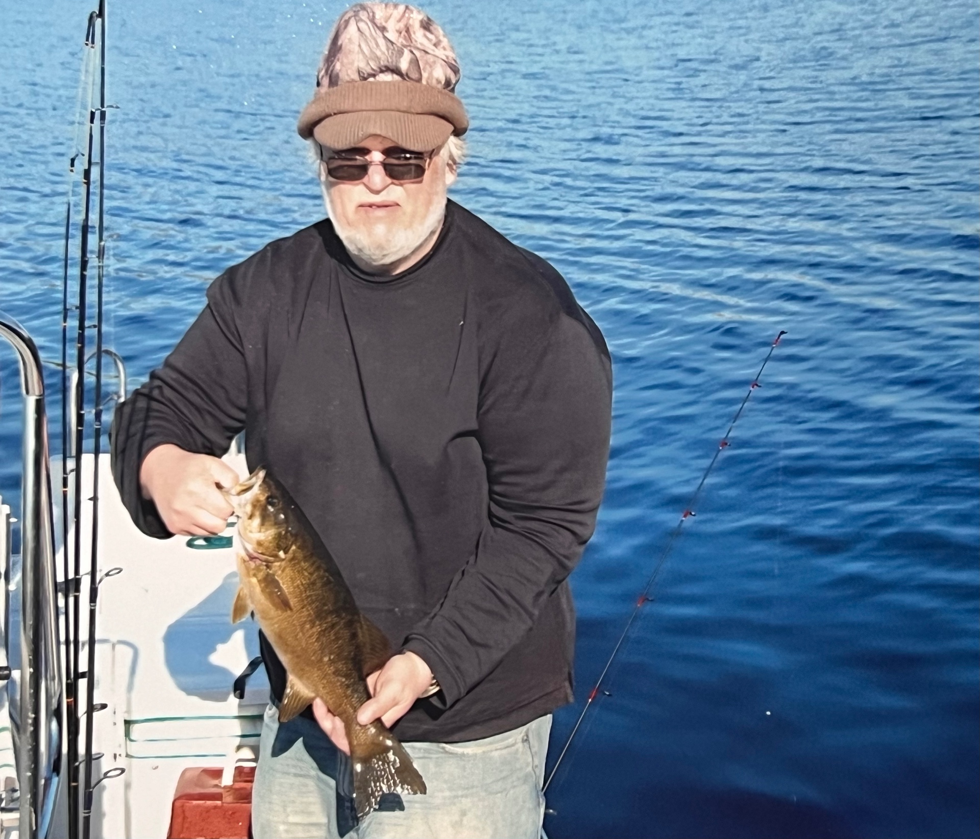 Richard on the boat with a beautiful smallmouth bass — deep blue water, camo cap, pure Canada