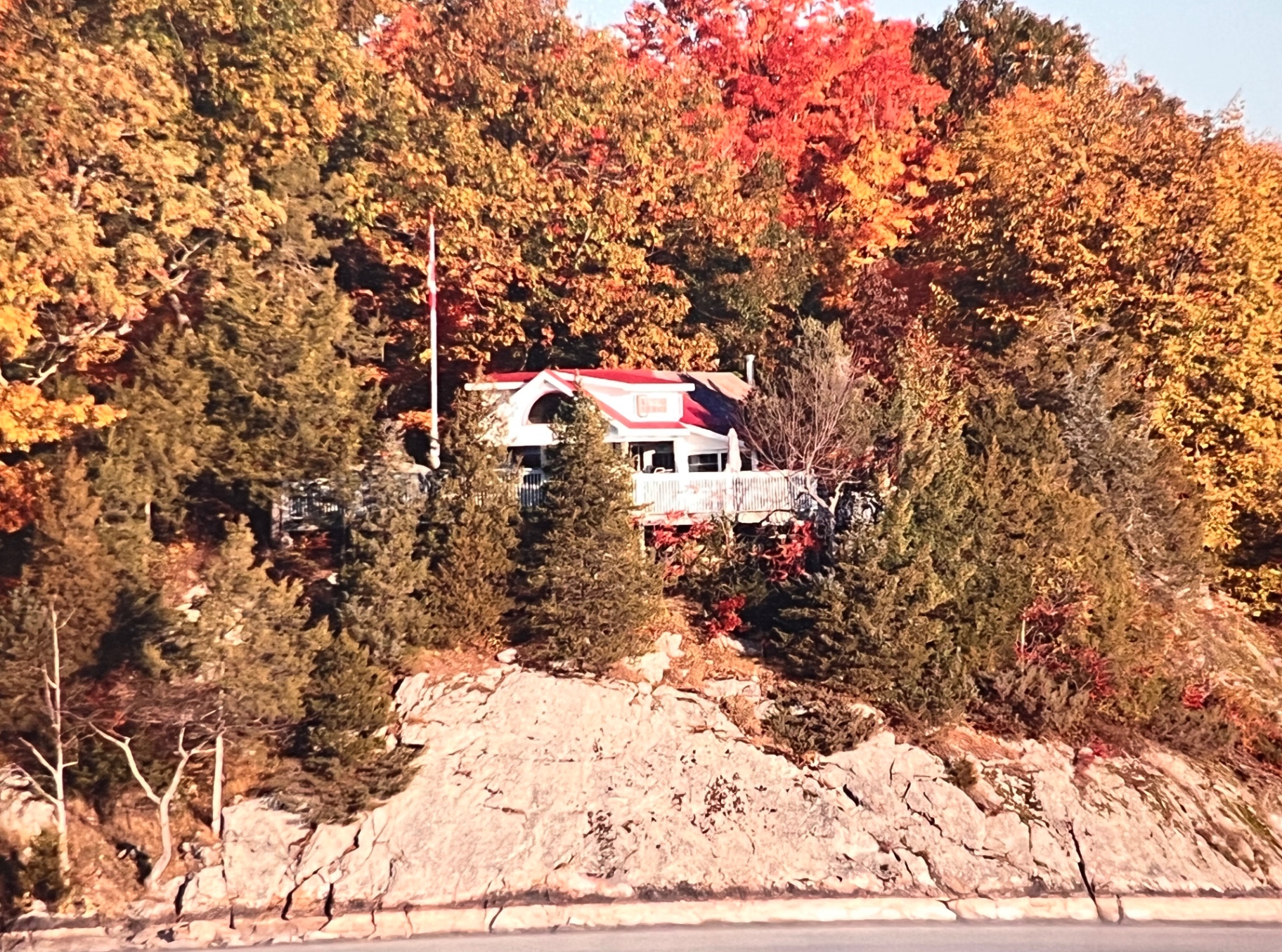 The cabin on the rocks — Canadian flag flying high above the maples, the kind of view Richard chased every fall