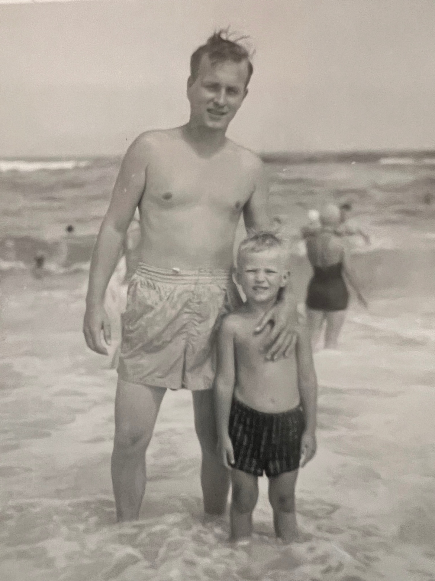 At the shore with Dad — arm around his boy, waves at their feet