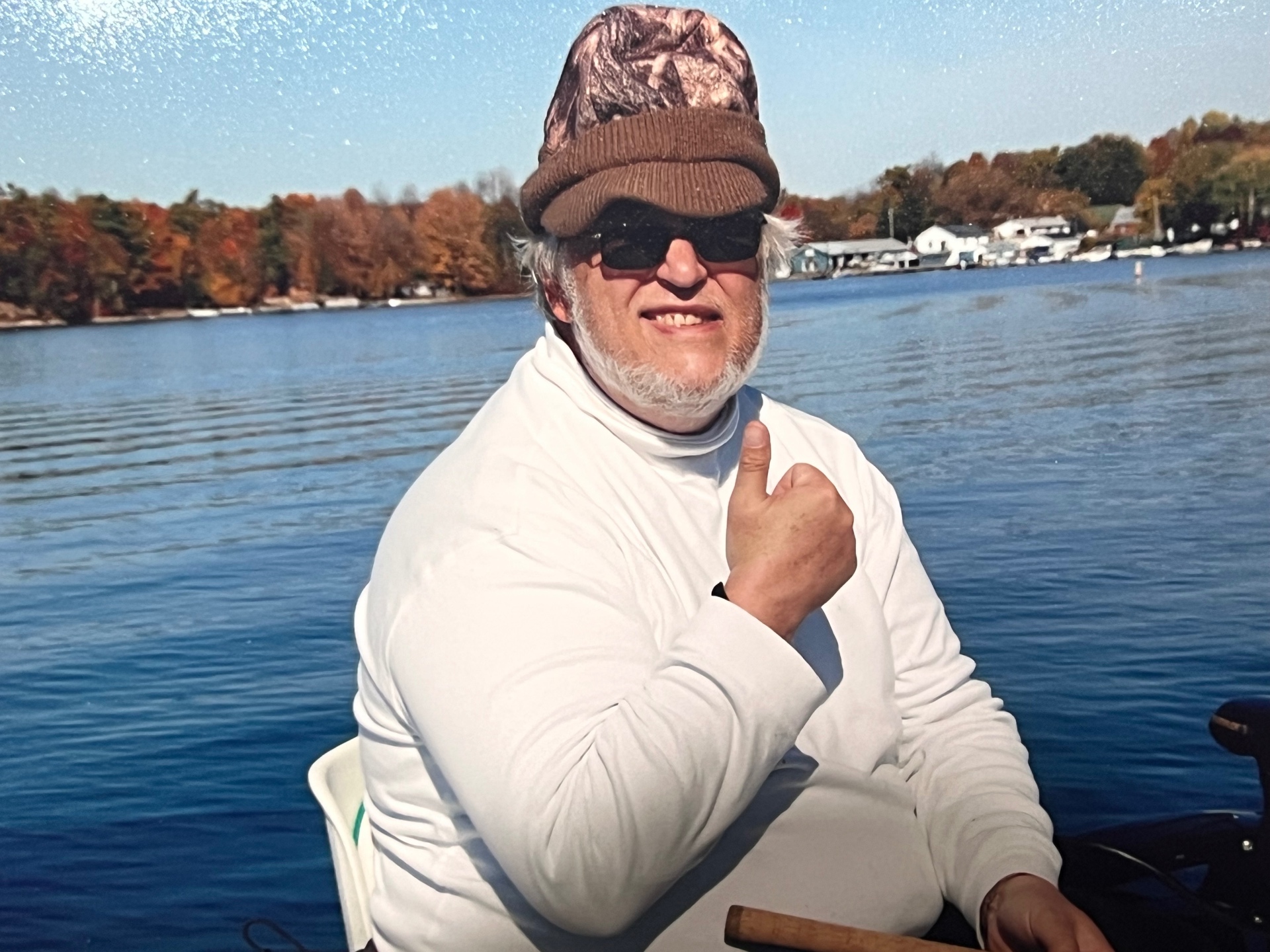 Richard on the boat in his camo cap and shades — a thumbs-up from the water, autumn colors lining the far shore