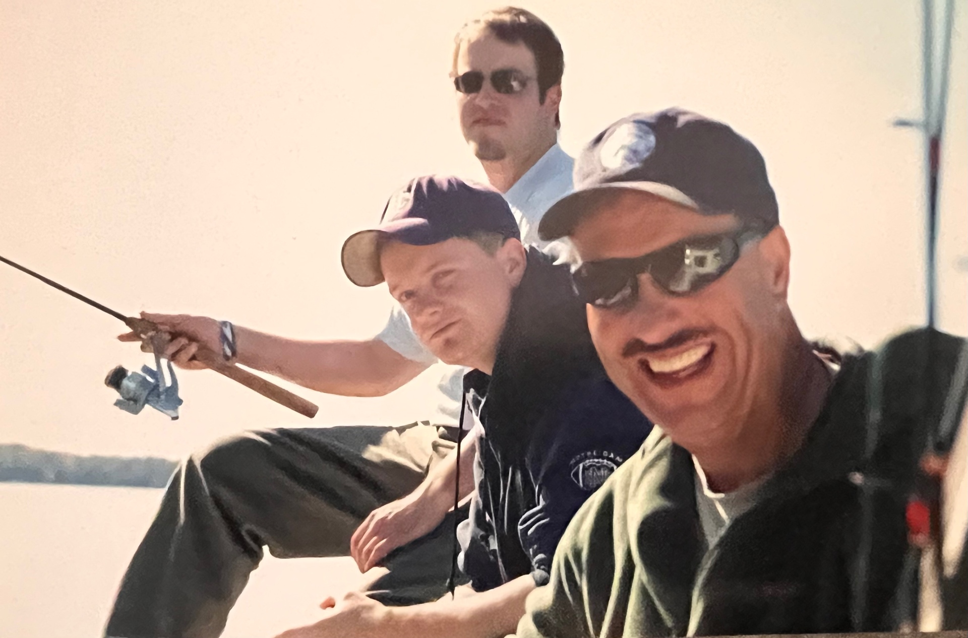 Three generations of grins on the boat — Richard up front with the boys, rods rigged, glassy water behind them