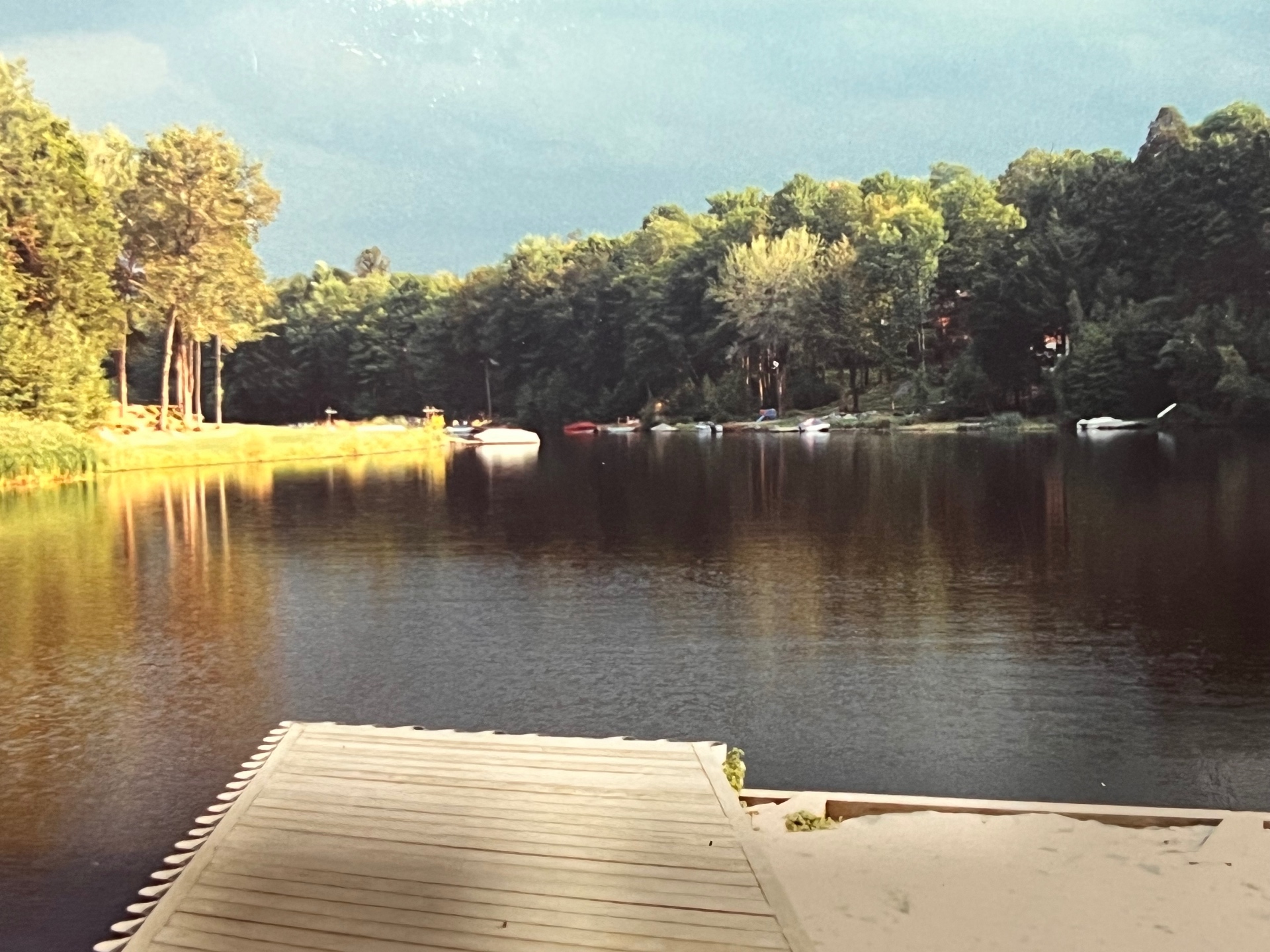 The view from the Hideout dock — golden light on the lake, boats along the far shore, the world Richard built quiet down to