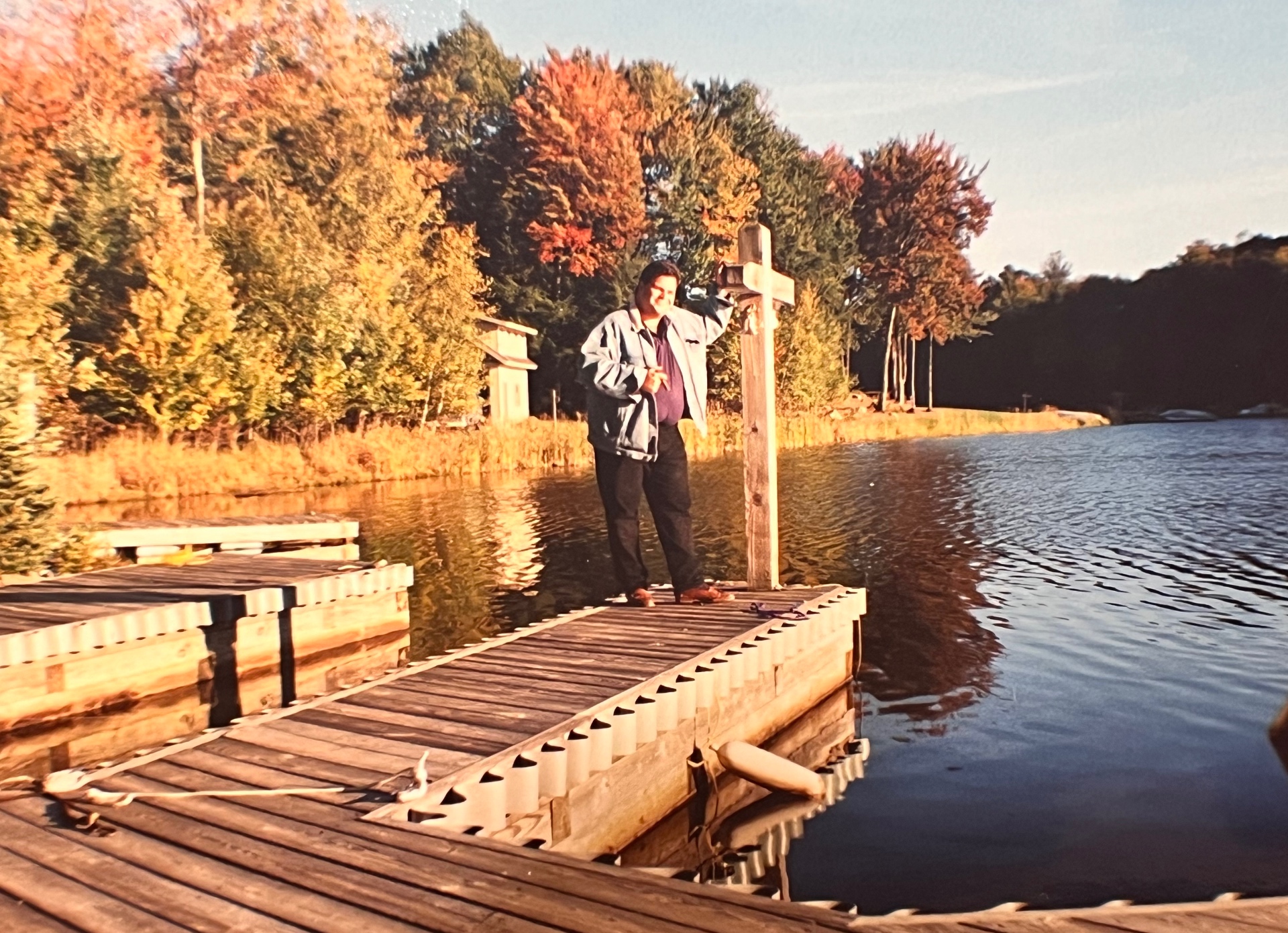 Richard on the dock beside the wooden cross — autumn on the lake, the light he loved best