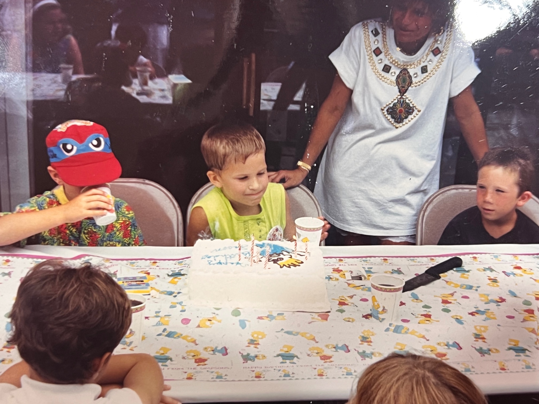 Simpsons tablecloth, buddies at his side, Yvonne standing proud behind him — a Bladis birthday in full swing