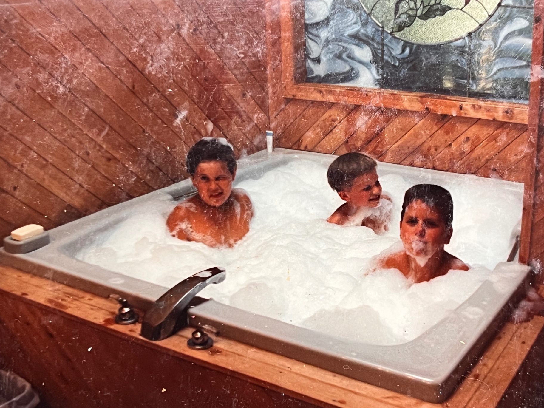Bubbles up to their chins in the big tub — cedar walls, stained glass, and three happy boys at The Hideout