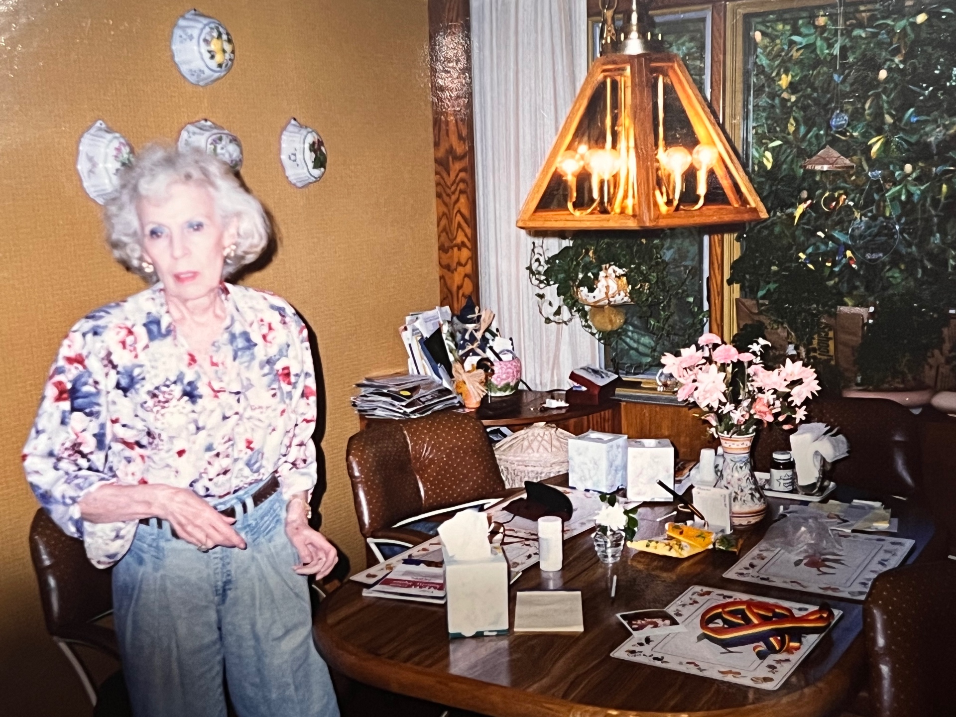 Grandma Gloria in her Christmas kitchen — cards on the table, tree glowing behind her