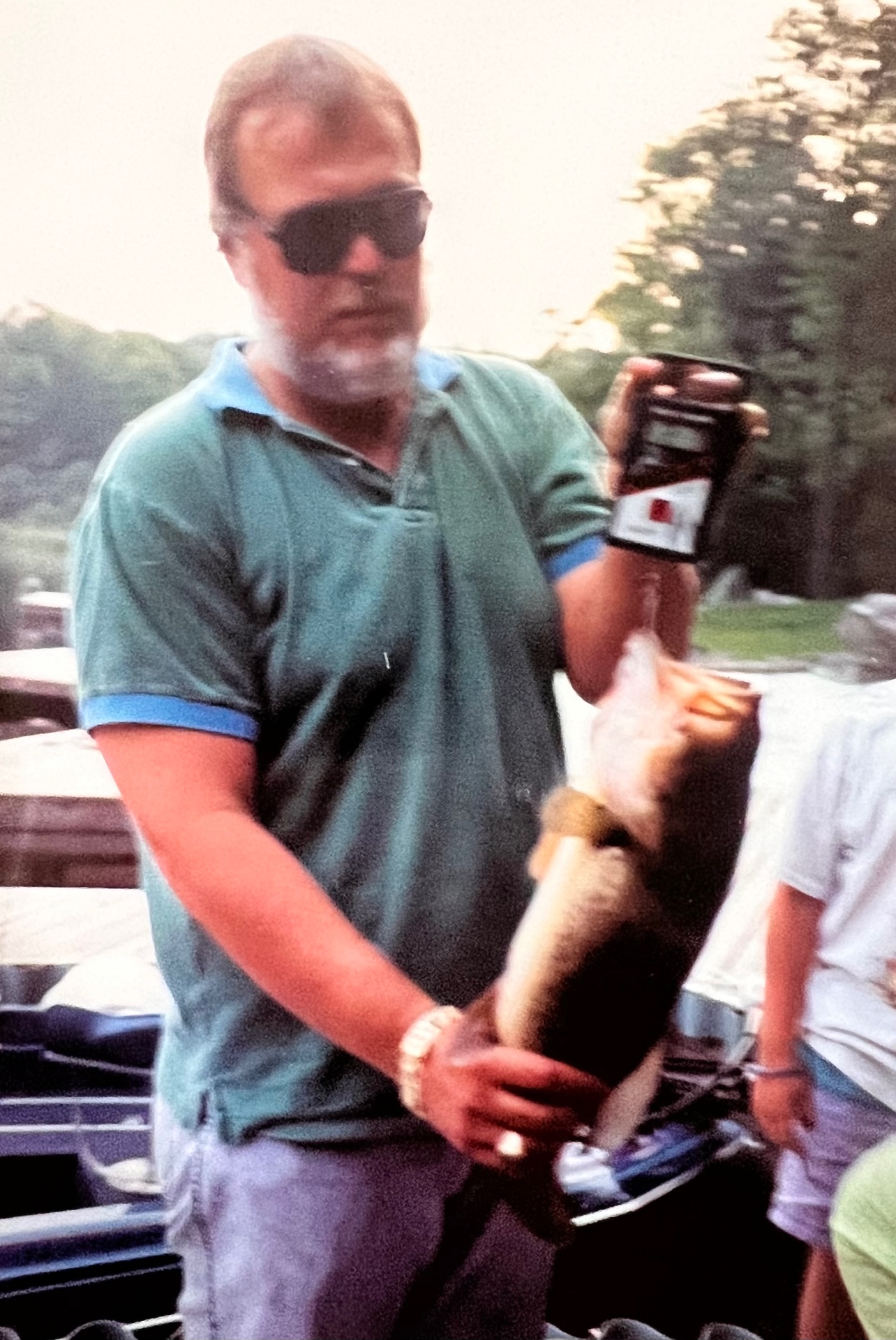 Always chasing the next big one — Richard at the dock with a solid largemouth in one hand, beer in the other, the lake behind him. Exactly where he wanted to be