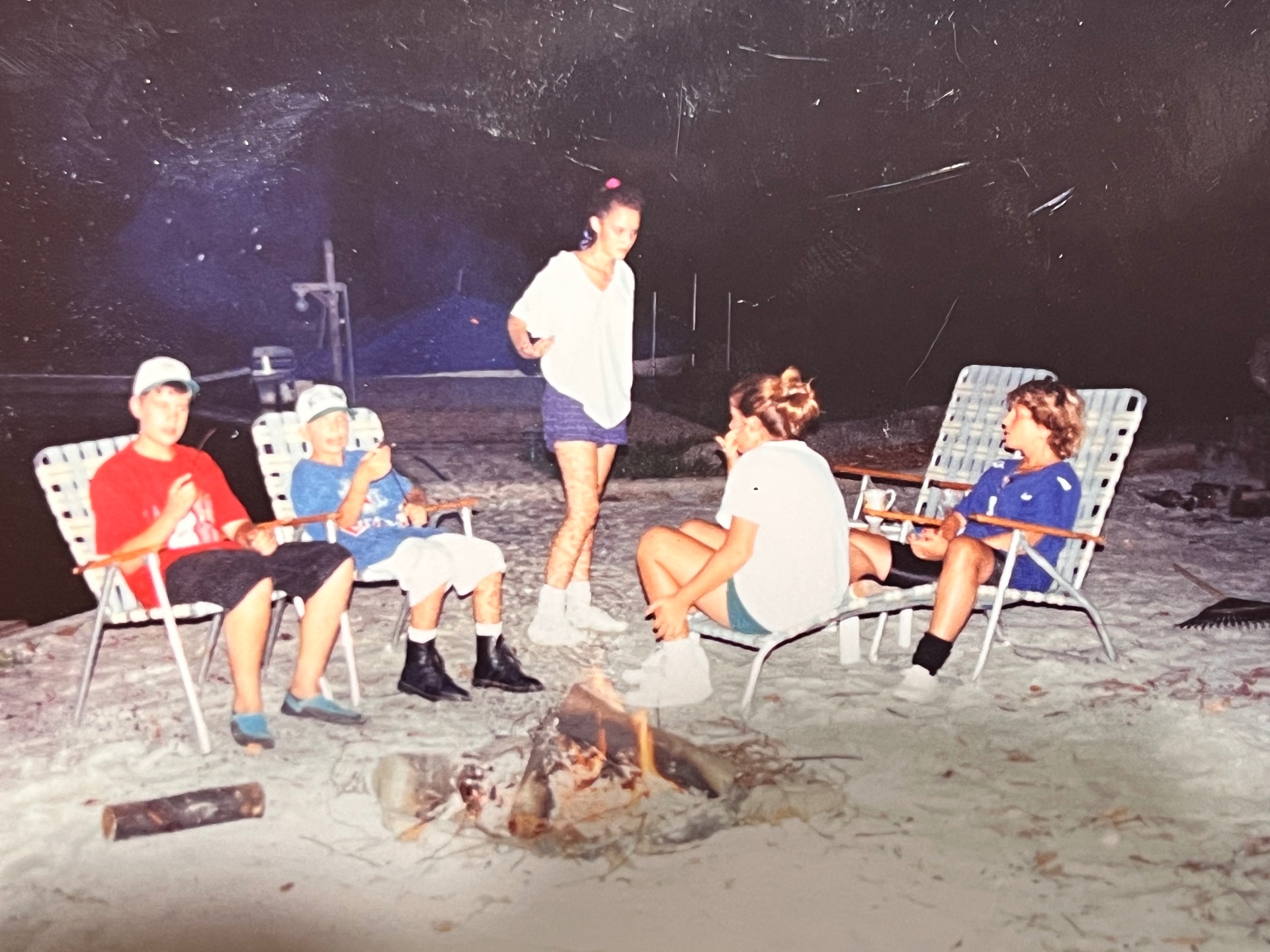 The whole crew around the Hideout firepit — sand under their feet, embers in the air, the lake dark and quiet behind them. Unforgettable Hideout nights