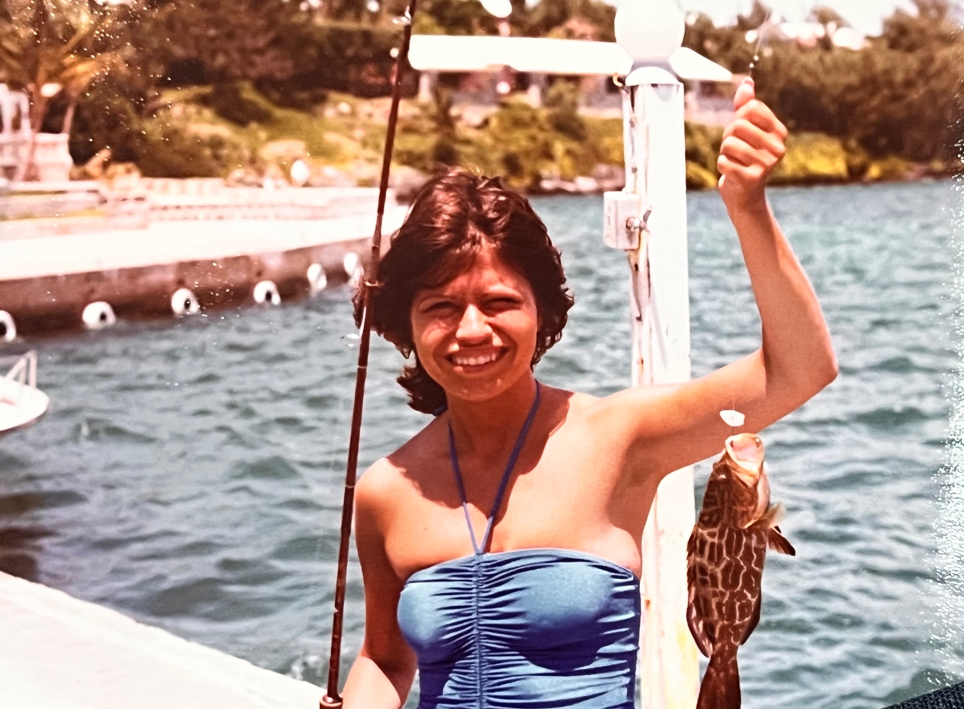 Yvonne on the dock in Bermuda, holding up a grouper — bathing suit, big smile, matching her husband cast for cast