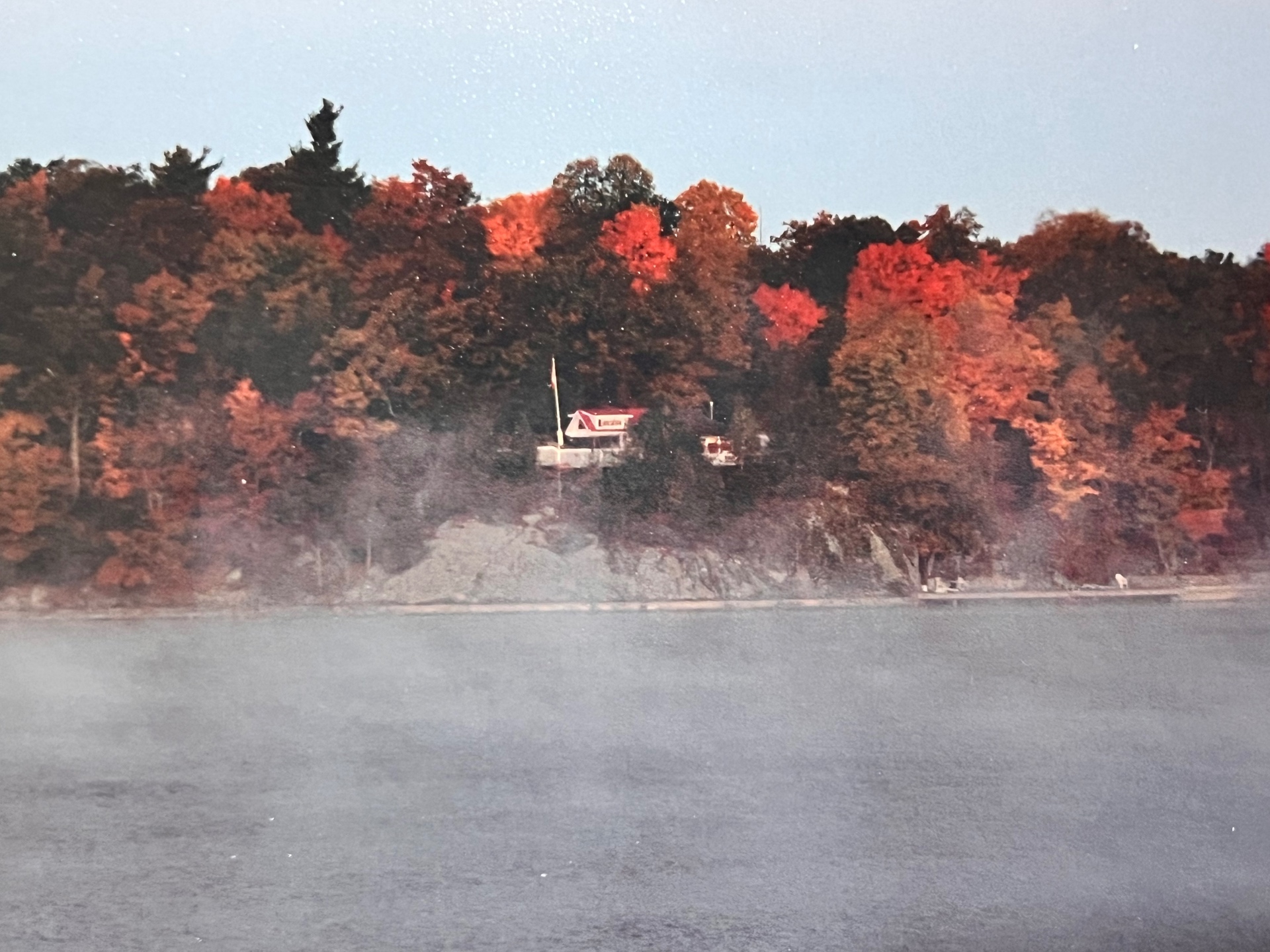 Mist rising off the water at dawn — the little red-roofed cabin on the cliff, quiet before the day's first cast